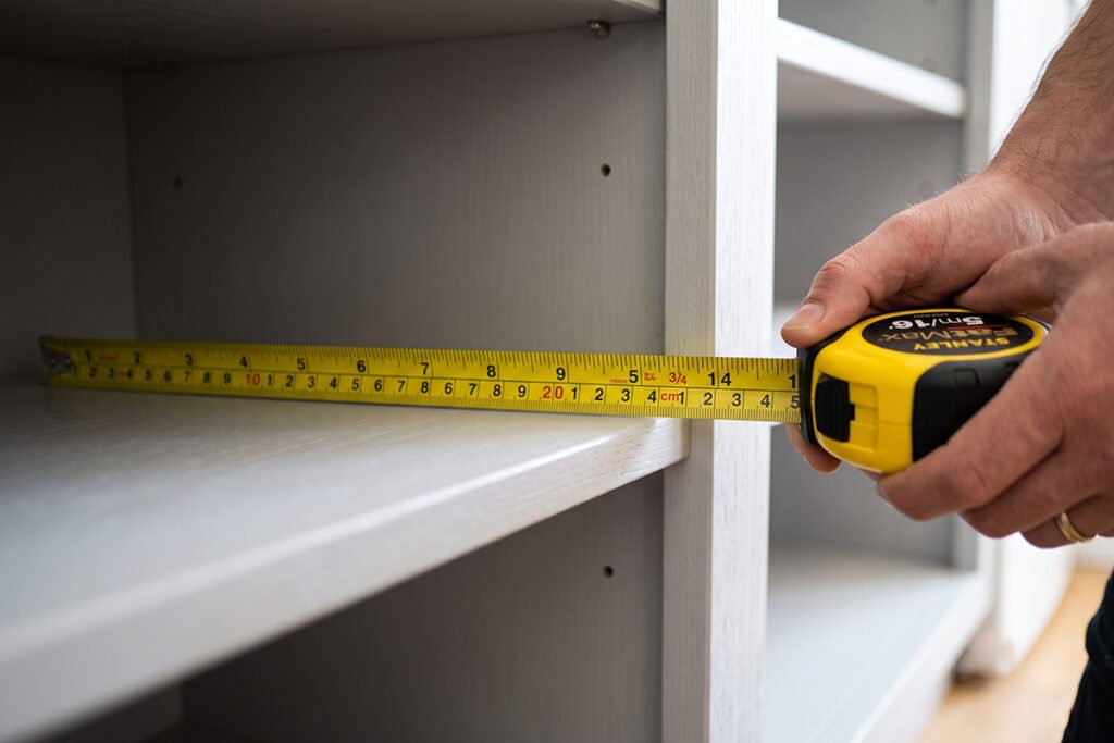 A tape measure checking the internal depth and width of an open kitchen base cabinet shelf.