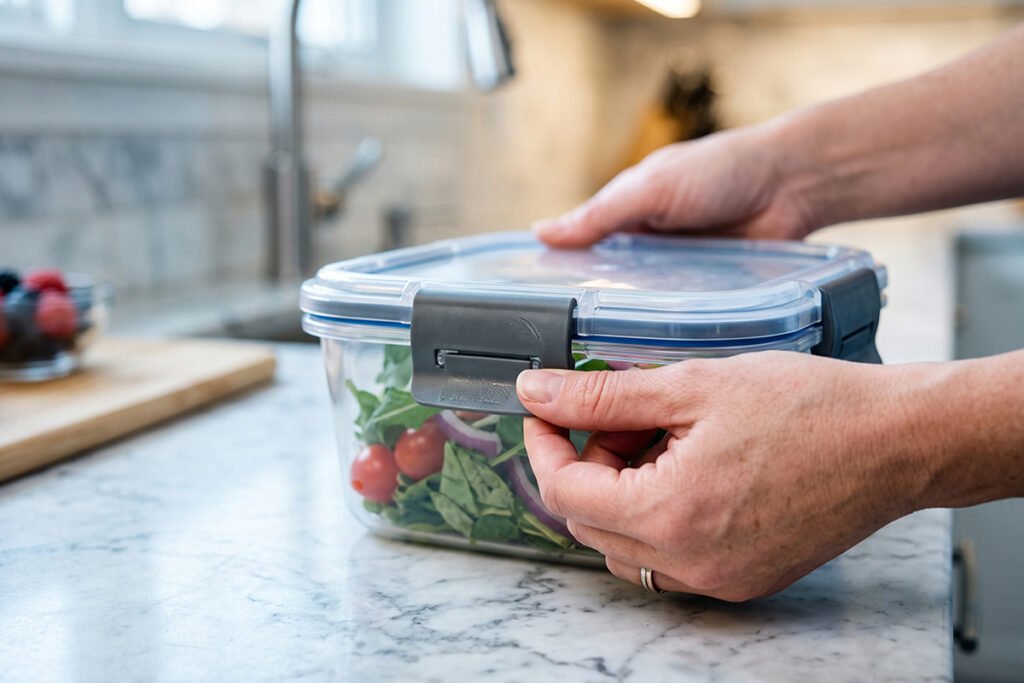 Close-up of a plastic food container with side-locking leakproof latches being secured in a kitchen.