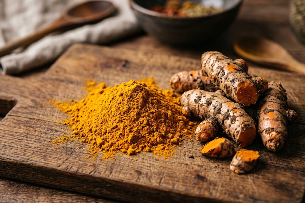Golden turmeric powder alongside fresh turmeric root on a rustic wooden board