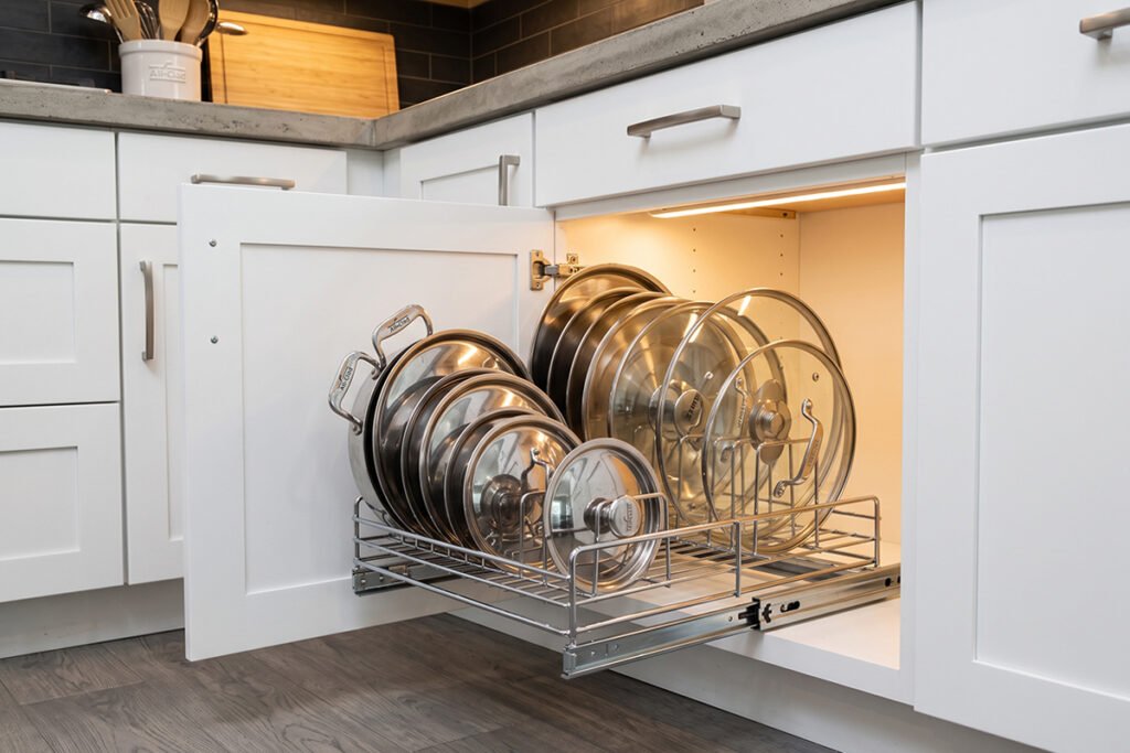 Lower kitchen cabinet equipped with a smooth pull-out chrome rack holding various saucepan lids upright